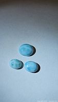 Photo showing the back side of three polished natural Larimar stones of different sizes on white background with shadow.