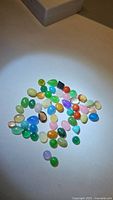 Top-down photo of mixed cabochon gemstones of various colors and sizes arranged loosely on white surface under light.