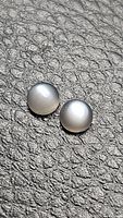 Pair of round natural moonstone cabochons with pearly flash, shown on textured black surface, displaying smooth domed surfaces and subtle adularescence.