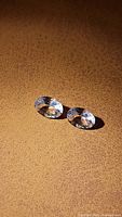 Pair of oval cut Morganite gemstones placed on textured light brown surface showing facets and internal clarity.