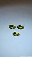 Three natural apple green peridot oval gemstones laid out on a white background, showcasing their color and cut.