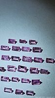 Multiple natural pink sapphires in baguette cut, arrayed in groups on a flat surface, showcasing rectangular shape, pink color, and clear facets.