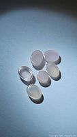 Six natural oval and round rose quartz cabochon stones displayed on light background with shadow cast