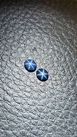 Pair of natural blue star sapphire oval cabochons showing the six-ray star effect on black textured background.