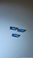 Three natural Swiss blue topaz gemstones arranged on a flat surface under direct light showing their rectangular faceted cuts and bright blue color.