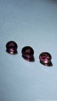 Three cabochon tourmaline gemstones in a row photographed against light background showing their color, clarity, cut shape and size.