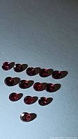 13 natural untreated noble red spinel gemstones laid out on a white surface with light casting shadows, showing their red color and diamond cut faceting.