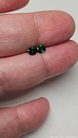Pair of small oval vivid green tsavorite garnet gemstones held between fingers for scale.
