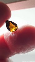 Pear cut deep cognac yellow tourmaline gemstone held against light, emphasizing color and facets.