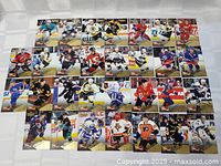 Photo showing 30 hockey cards arranged in 5 rows of 6 cards each, featuring players on ice in action shots with team uniforms and gold-bordered design.