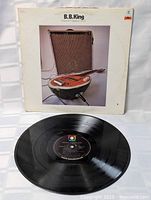 Photo of the vinyl LP disc alongside the album cover showing the front artwork featuring an amplifier and a guitar.