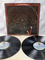 Photo of the album cover with two vinyl records partially visible in front. Cover shows typical wear such as creases and scuffs.