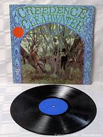 Vinyl record LP and original album cover showing band members outdoors around tree, cover art with blue decorative border and band title.