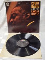 Photo showing the vinyl LP record partially pulled out of the inner paper sleeve and the front album cover standing behind. The cover features a close-up side profile photo of Count Basie with text in yellow and white on a dark background.