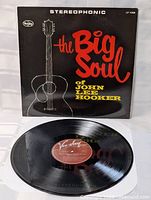 Photo showing the vinyl record on a white paper inner sleeve with album cover behind it. The label on the record is visible, showing Vee Jay Records branding with text consistent with John Lee Hooker's album.
