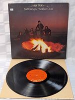 Front cover of the Northern Lights - Southern Cross album by THE BAND showing band members around a campfire at dusk, with some typical aging wear and a price sticker.