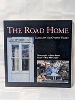 Front cover of the book titled 'The Road Home: Images of the Ottawa Valley' showing a photo of a window with sign 'The Opeongo Line' and a color photo of people sitting with a dog.