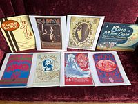 Six vintage cultural posters and two vintage tin signs displayed on a red couch, front view showing design details and text.