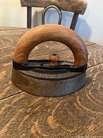 Close-up image of antique sad iron with wooden handle on wooden table showing side view with visible maker marks and patina.