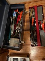 Two metal toolboxes open displaying assorted hand tools including pliers, screwdrivers, adjustable wrenches, combination wrenches, sockets, and other small tools.