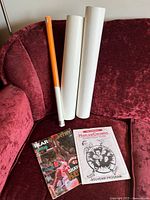 Three posters rolled and two catalogues/programs placed on red velvet chair.