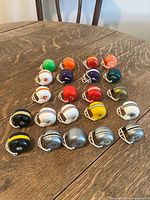 Photo of 21 miniature NFL helmets arranged on a wooden table, showing diverse team colors and logos including Browns, Ravens, Bears, Packers, Steelers, and Raiders.