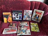 The full lot arranged on a red textured fabric couch including vintage comics, books, magazines, and a VHS tape.