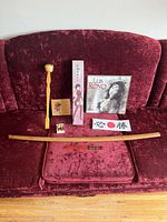 Photo showing the full lot arranged on red sofa: wooden katana, poster/calendar of Luis Royo artwork, fabric head band with Japanese characters, red and gold chopsticks, wooden back scratcher, greeting card, small box.