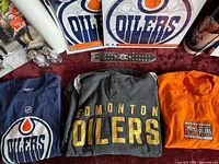 Edmonton Oilers shirts, bracelets, and two mini Stanley Cups displayed on red upholstery.