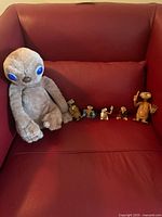 Red couch with single ET plush and five small ET figurines lined up, showing size and variety.