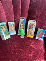 Six hula dolls arranged on a red velvet backdrop, including two promotional dolls and most dolls in original packaging.