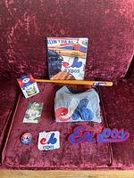Montreal Expos T-shirt, patches, postcard, small bat, duotang displayed on pink fabric surface