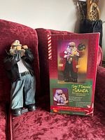 Photo of Santa figure playing saxophone in original box, wearing dark leather jacket with 'HO HO HO' on the back
