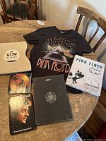 Photo showing Pink Floyd t-shirt, Pink Floyd books including "Behind the Wall" and a book with prism and pig graphics, and three other music-related books including Johnny Cash