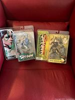 Photo showing three Spawn action figures in original packaging placed on a red chair.