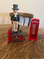 Uncle Sam and British phone booth piggy banks on wooden table.