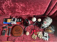 Image showing multiple baseball gloves, balls, and a hit-a-way training mitt laid on a red surface.