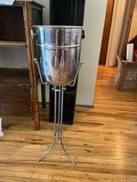 Metal tableside wine chiller with polished finish on tall tripod stand