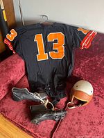 Black King O’Shea football jersey with number 13 displayed on red couch alongside Wilson helmet and Hotshot Continental cleats.