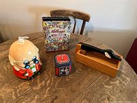 Photo of the full lot on a wooden table showing the cookie jar, Kellogg's tin, Planters tin, and goose nut cracker