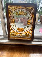 Front view of orange-brown stained glass window panel featuring lotus flowers in circular design set in a wooden frame.
