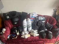 Hockey pads, gloves, helmet protector, socks, and accessories laid out on red couch.