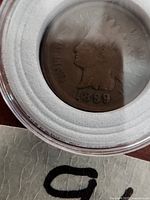 Obverse side of the 1899 Indian Head penny in protective casing showing the profile of Lady Liberty with a Native American feather headdress and the date 1899