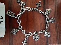 Full view of the silver charm bracelet showing all attached cross-themed charms laid out on a wooden surface.