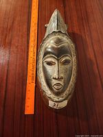 Front view of the African carved wooden face mask with ruler alongside for size reference.
