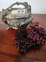 Antique pewter jewelry box shown closed with berry napkin holders beside it on table.