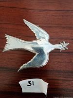 Top view of silver dove figurine with wings spread, showing polished surface and branch detail.