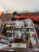 Plastic tray containing two satin nickel finished door knobs, two separate latches, and accompanying keys with part of a red hammer visible above.