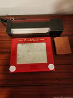 Etch A Sketch, car emergency flash light, and small brown wallet arranged on wooden surface