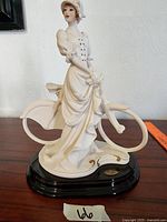 Full side view of the porcelain statue showing the woman in vintage attire on the bicycle with black base.